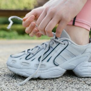 Close-up of a woman tying shoelaces on white sneakers during an outdoor exercise session.